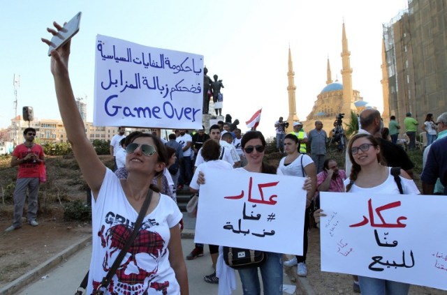 Lebanese young women take pictures as they hold placards before the start of an anti-government protest organised by a civil society frustrated with a political class they see as corrupt and incapable of providing basic services on August 29, 2015 at Beirut's iconic Martyrs Square. "Today, we're expecting more than 50,000 protesters," said Assaad Thebian of the "You Stink" which is stressing the non-partisan nature of the demonstration. The placards read "Akkar is not for sale (C and R) and "Game over you government of political trash"(L). AFP PHOTO / ANWAR AMRO